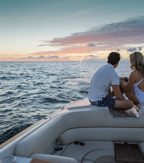 A couple sits on a boat in the ocean with the sun