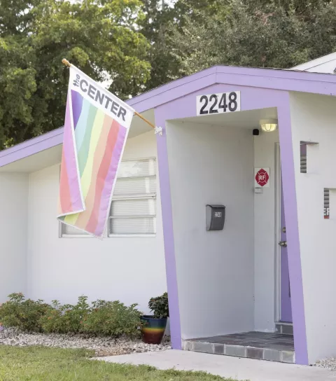 Exterior image of a small white house with purple trim and a rainbow flag that reads "The Center."