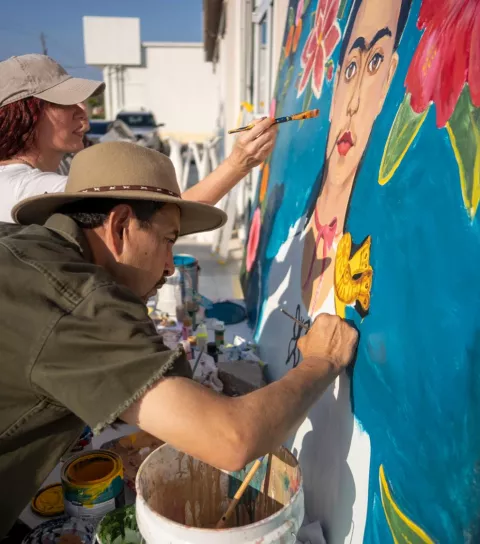 Group of people paining a mural of Frida Kahlo