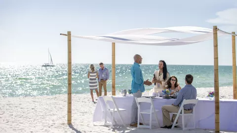 Four people sit at a table under a canopy, two peo