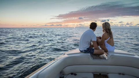 A couple sits on a boat in the ocean with the sun A couple sits on a boat in the ocean with the sun