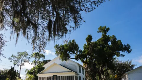 A white house with a covered porch with trees surr A white house with a covered porch with trees surr