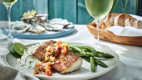 A plate of seafood sits on a table next to a glass