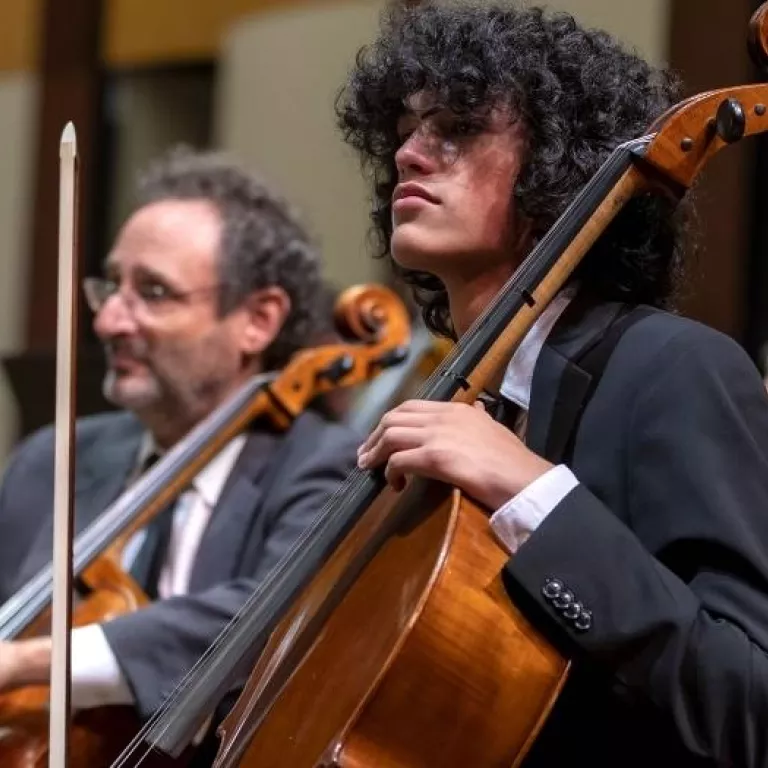 Image of youth musicians of the Naples Philharmonic Youth Orchestra playing side by side with musicians of the Naples Philharmonic on stage during performance Photo