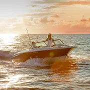 A couple rides a speedboat on the ocean at sunset.