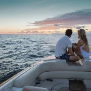 A couple sits on a boat in the ocean with the sun