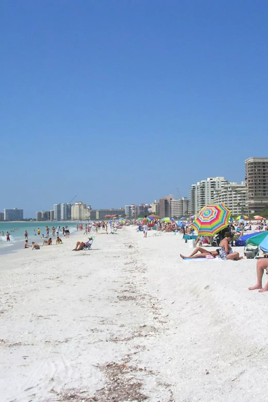 Beachgoers with colorful umbrellas spread out on t