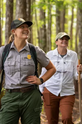 A park ranger and a hiker explore with trees in th